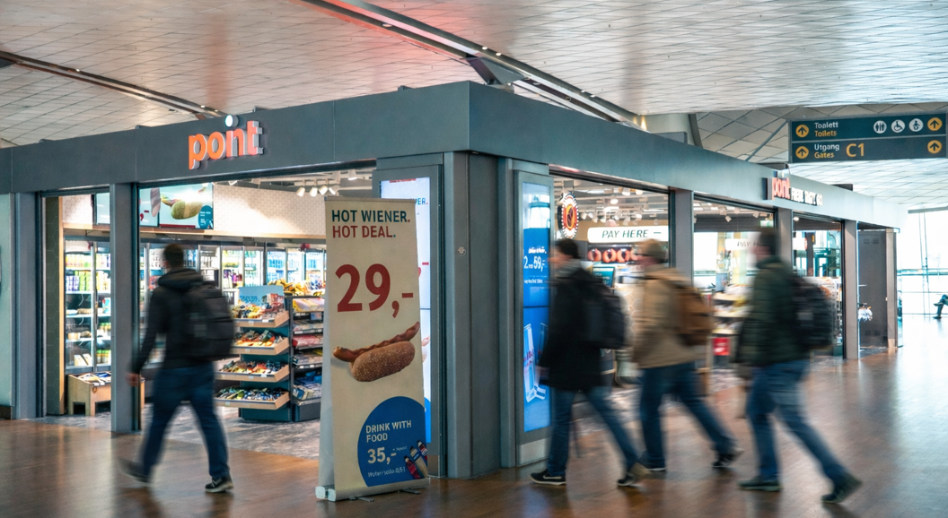 Smiling cashier in a blue uniform at a convenience store counter, with a promotional sign in the background