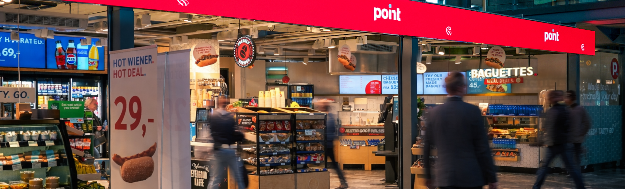 Butikkskilt på en flyplass med teksten "point" og "FRESH. TASTY. GO." vist over en butikk som tilbyr magasiner og bøker, med synlig takbelysning og skilt for reisemålporter