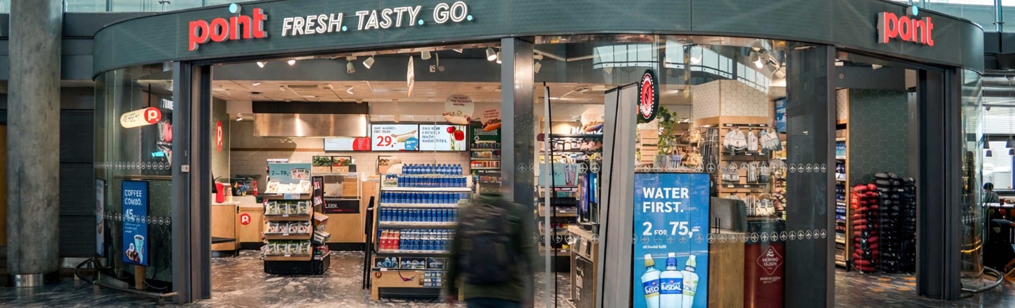 Butikk ved flyplass inngang med skiltet "Point: Fresh. Tasty. Go." Visning av produkter og mattilbud innendørs