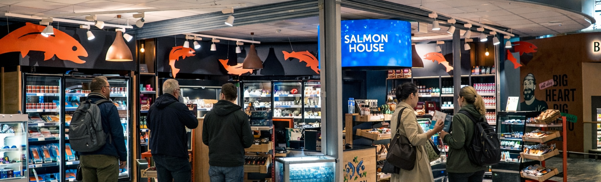 Logo for Salmon House med to stiliserte fisk omgitt av grønne blader og bær, med teksten "Salmon House" under i fete blå bokstaver