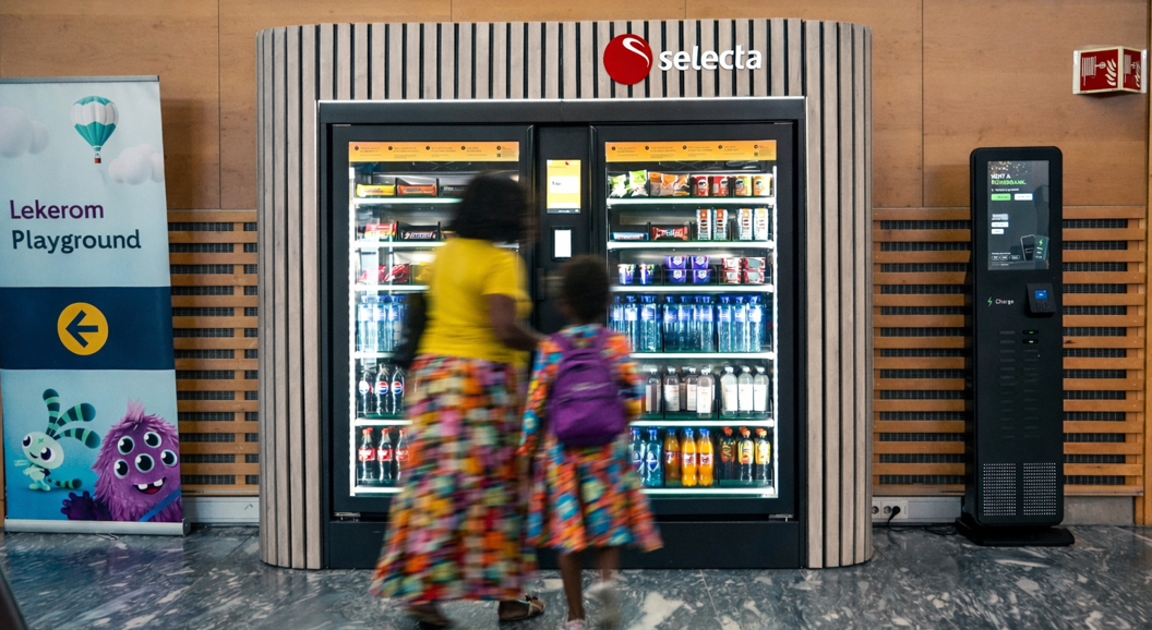 Automat fylt med assorterte snacks og sjokoladebarer, inkludert populære merker, med opplyst valgpanel