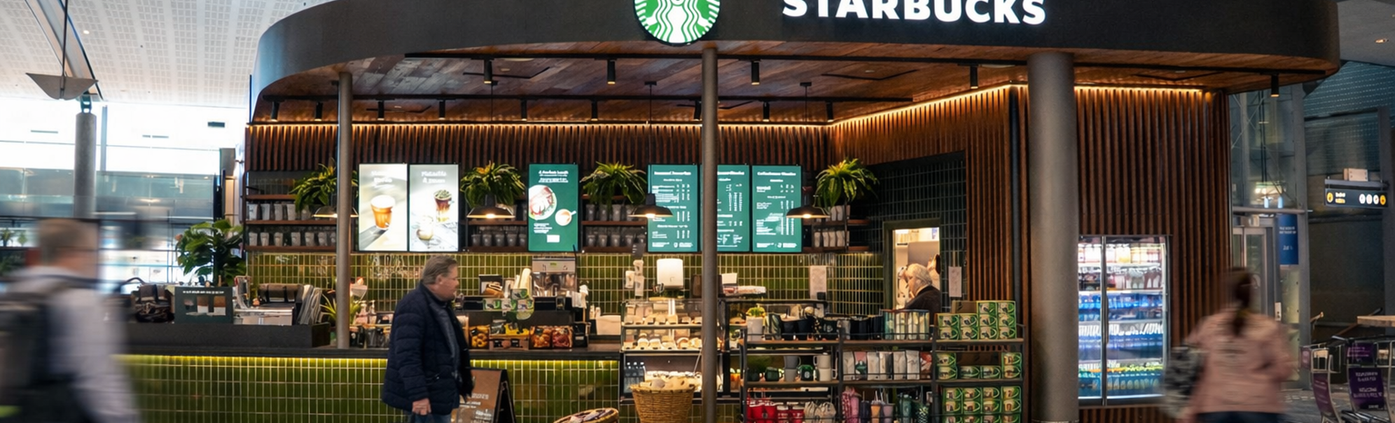 To personer ler og drikker kaffe ved et bord på en kafé. En kvinne har en grønn genser og en mann har en hvit t-skjorte. En Starbucks-logo vises på koppen