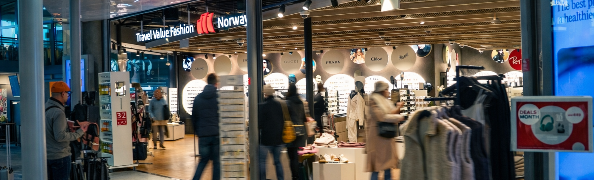 Kvinne som handler solbriller i en moderne butikk, iført en svart skinnjakke og smiler mens hun prøver et par solbriller