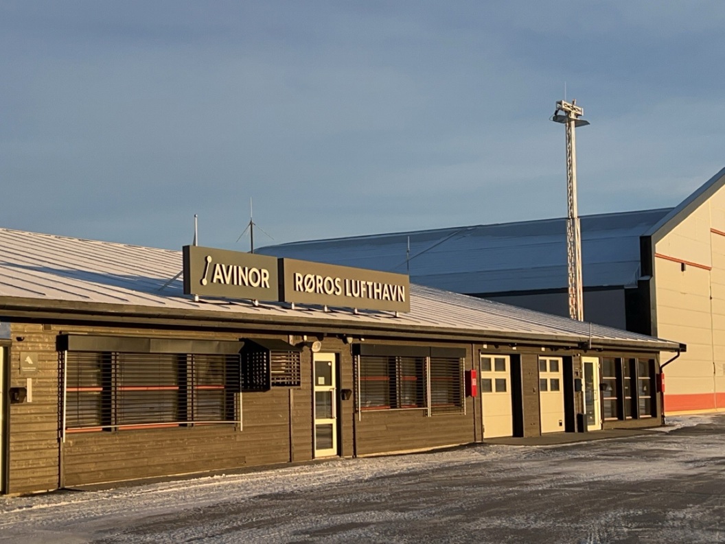 Kontrolltårn ved Røros flyplass med snø på taket, en parkeringsplass foran og en bil til venstre. Vinterlig landskap under klar himmel.