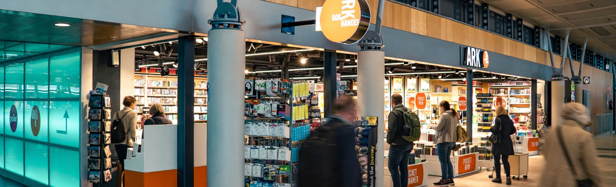ARK butikken inne i terminalen på Trondheim lufthavn, med mennesker som går utenfor.