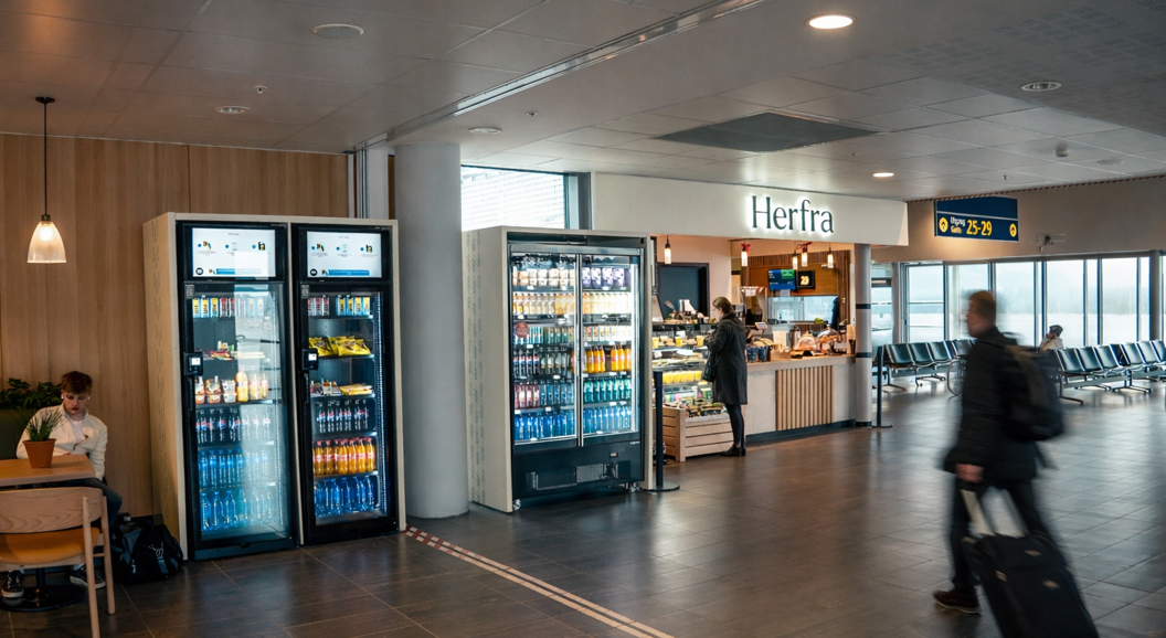 Flyplasskafé med kiosk, drikkeautomater og reisande i terminalen