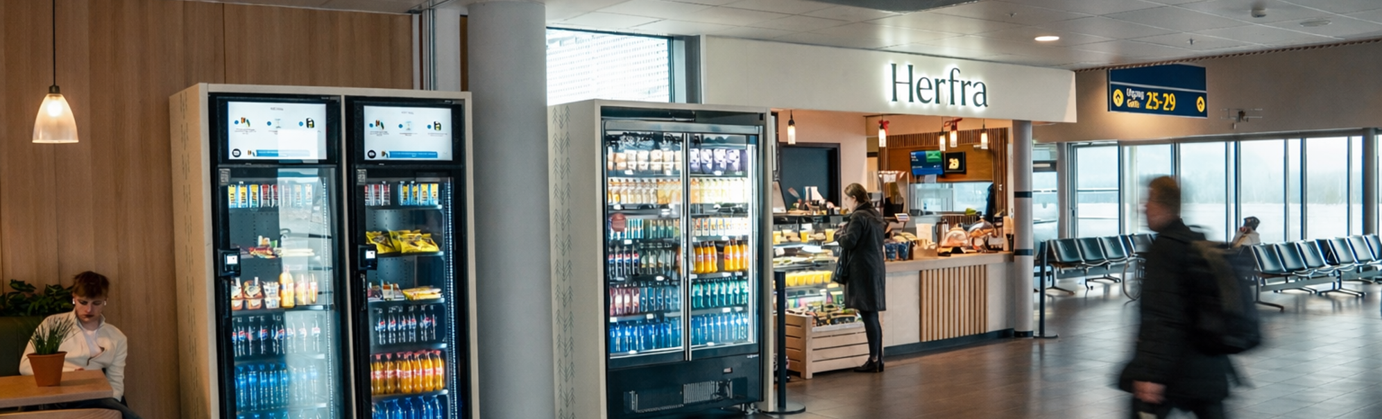 Flyplasskafé med kiosk, drikkeautomater og reisande i terminalen
