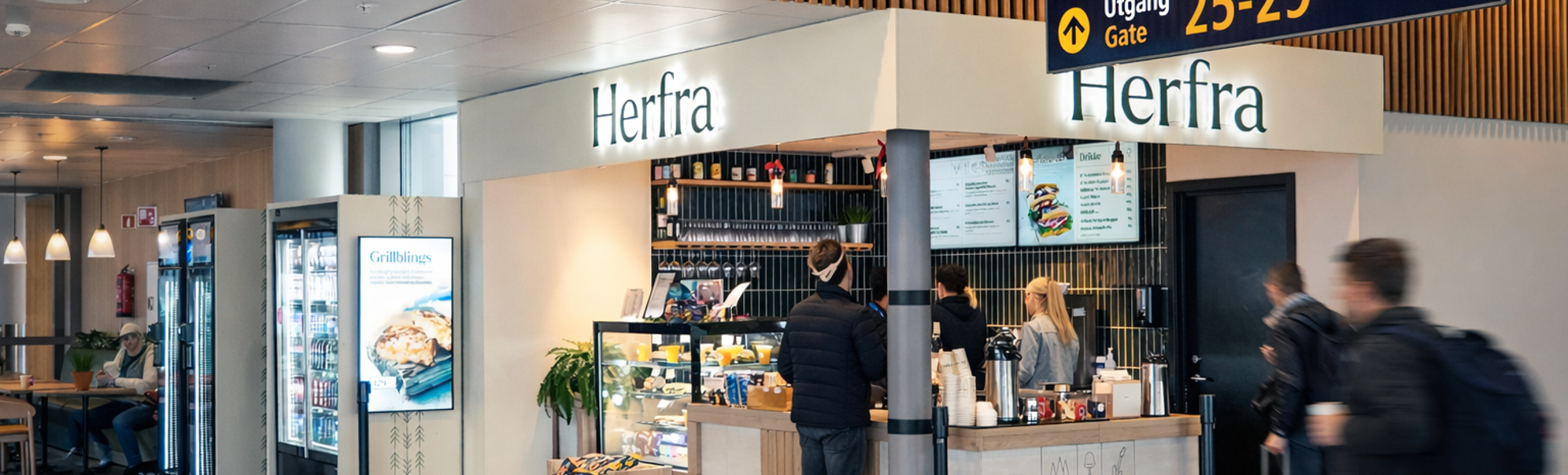 Flyplasskafé og snackbar ved navn Herfra nær gate 25–29, med reisende og bagasje i en terminalgang