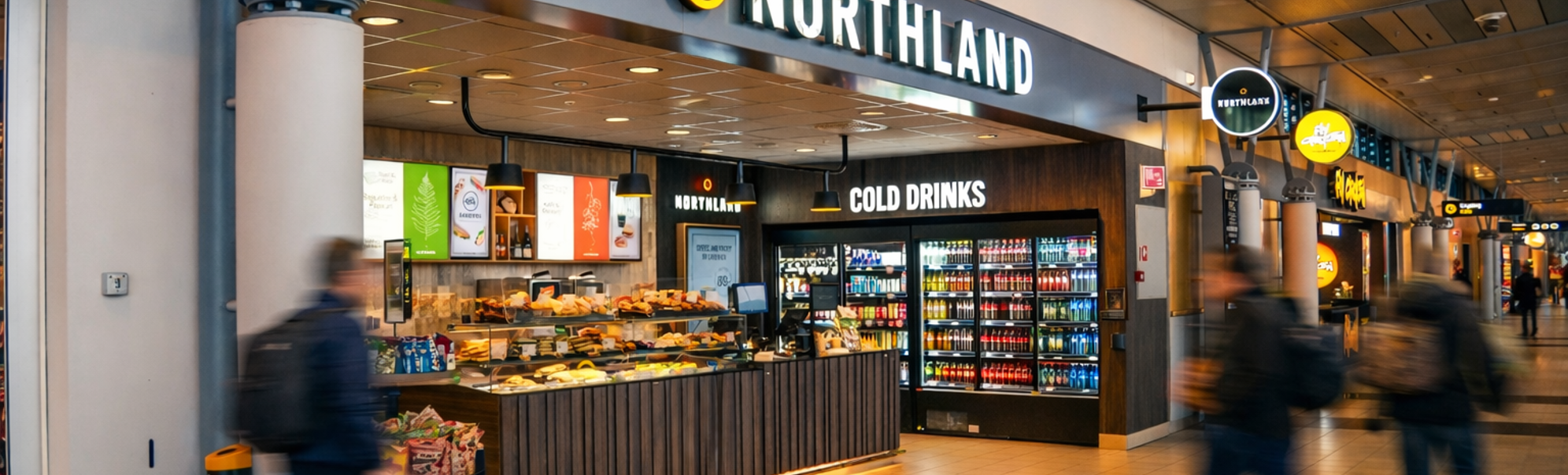 Northland flyplass-kiosk med snacks, kalde drikker og reisende som går forbi i en terminalkorridor