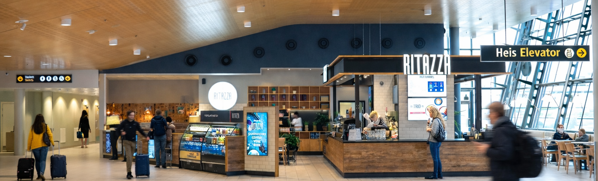 Moderne matområde på flyplassen med Ritazza-kaffekiosk, reisende og heiskilt inne i en romslig terminal