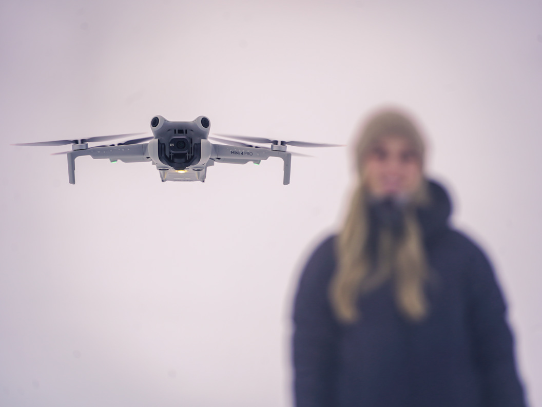En drone som svever foran en uskarp person mot en ensfarget bakgrunn